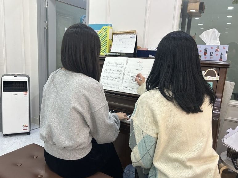 강사가 악보를 짚어가며 피아노를 1:1로 지도하는 모습